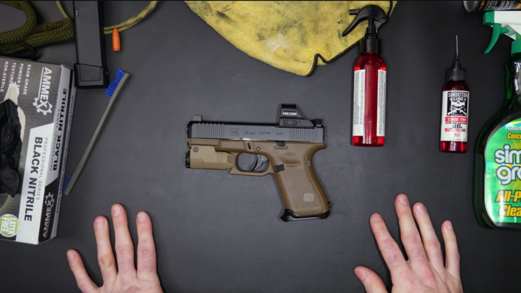 Man showing how to clean a Glock with gloves, brush, cloth and other cleaning products